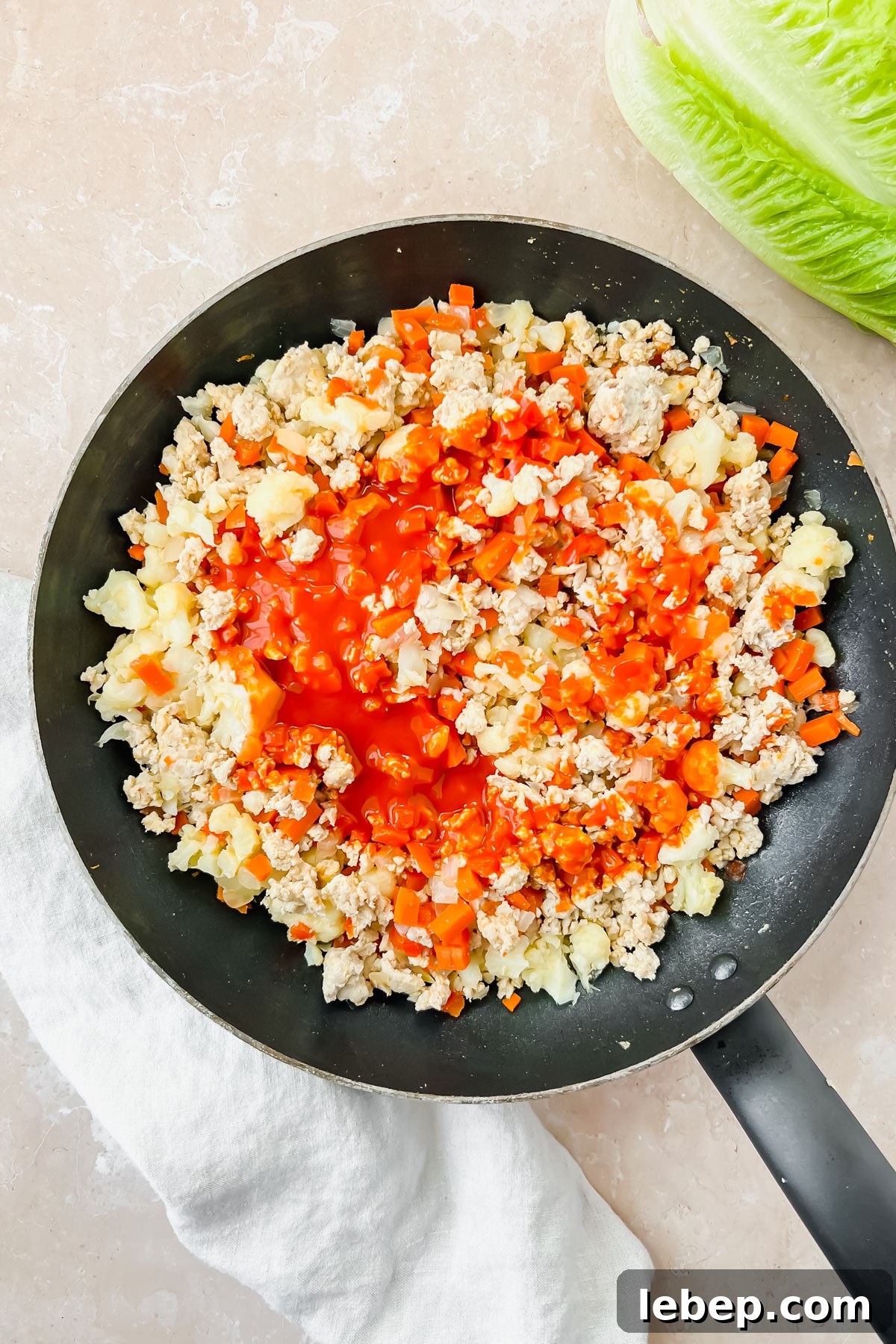buffalo cauliflower chicken mixture in black skillet with sauce added on top.