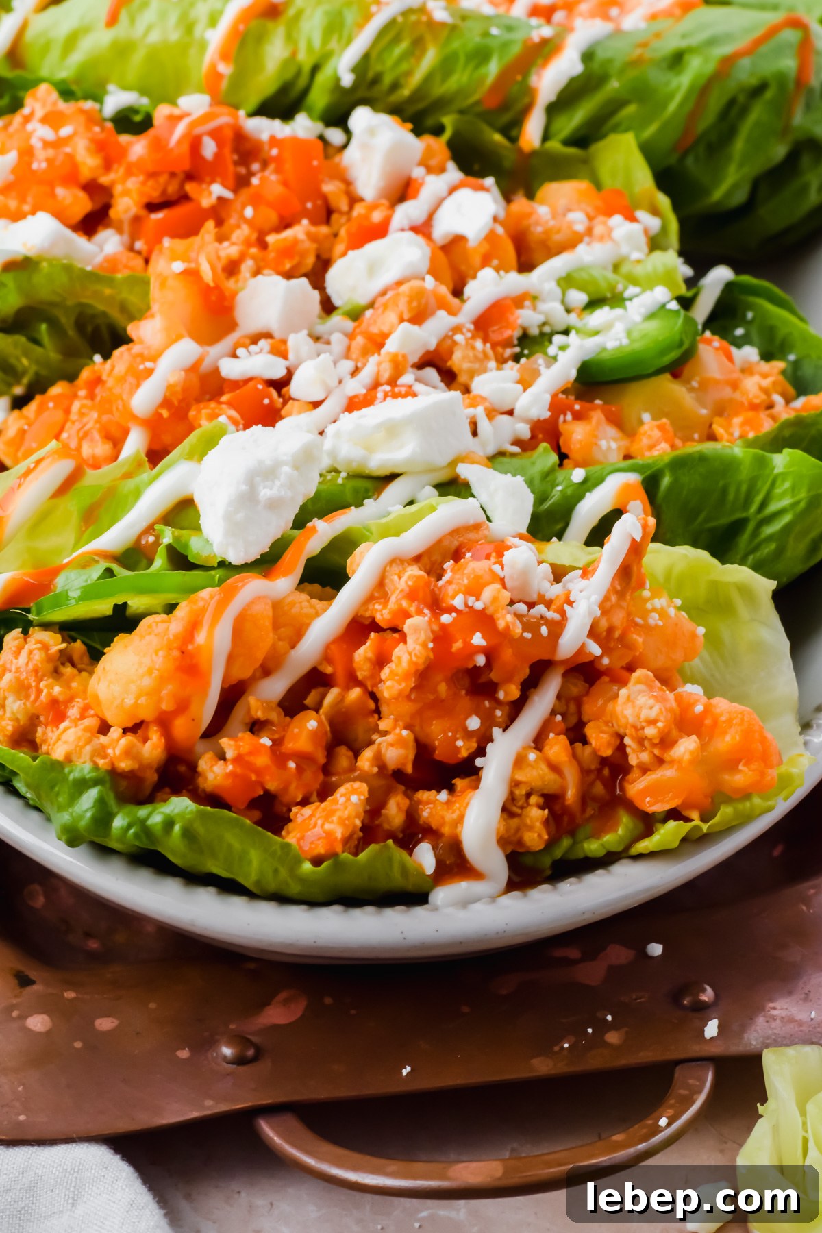 loaded buffalo cauliflower chicken lettuce wraps garnished with ranch and feta on white serving plate.
