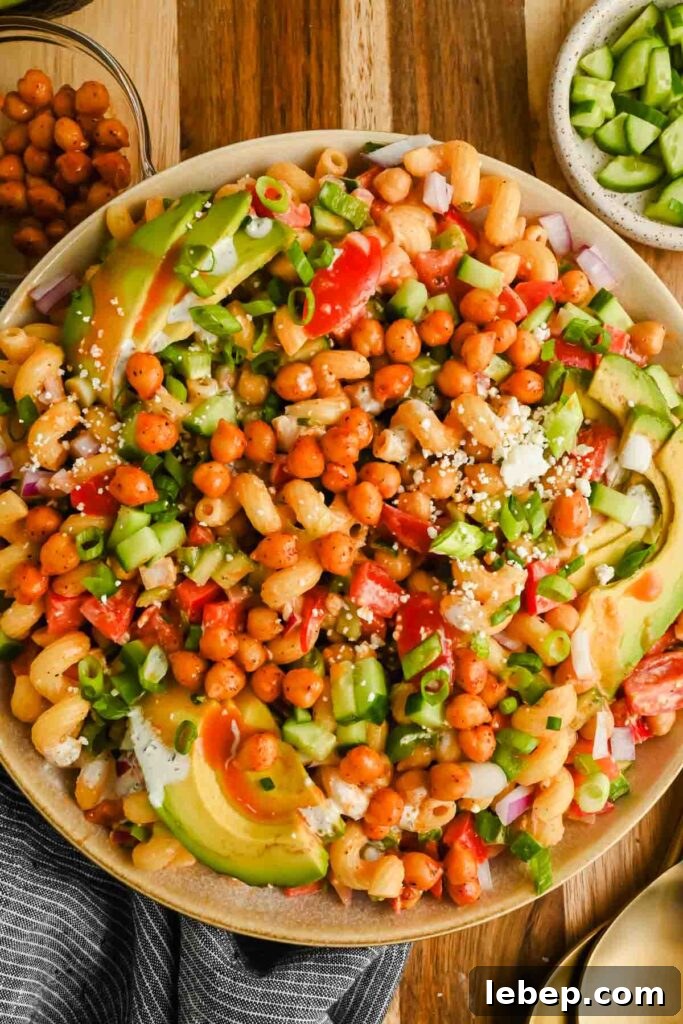 buffalo pasta salad garnished with chickpeas, green onions, avocado and feta in large serving bowl.