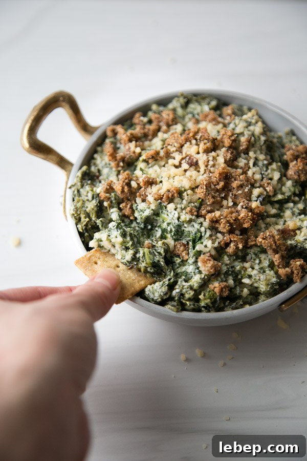 Creamy Warm Spinach Dip — Dairy- and Gluten-Free Recipe 2 hand dipping gluten-free cracker in dairy-free spinach dip