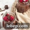 Two mason jars filled with chocolate pudding topped with raspberries.