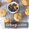 Paleo morning glory muffins on a cooling rack with a white bowl of blueberries and pecans.
