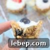 A close up image of two fingers holding a granola cup with yogurt and blueberry on top.
