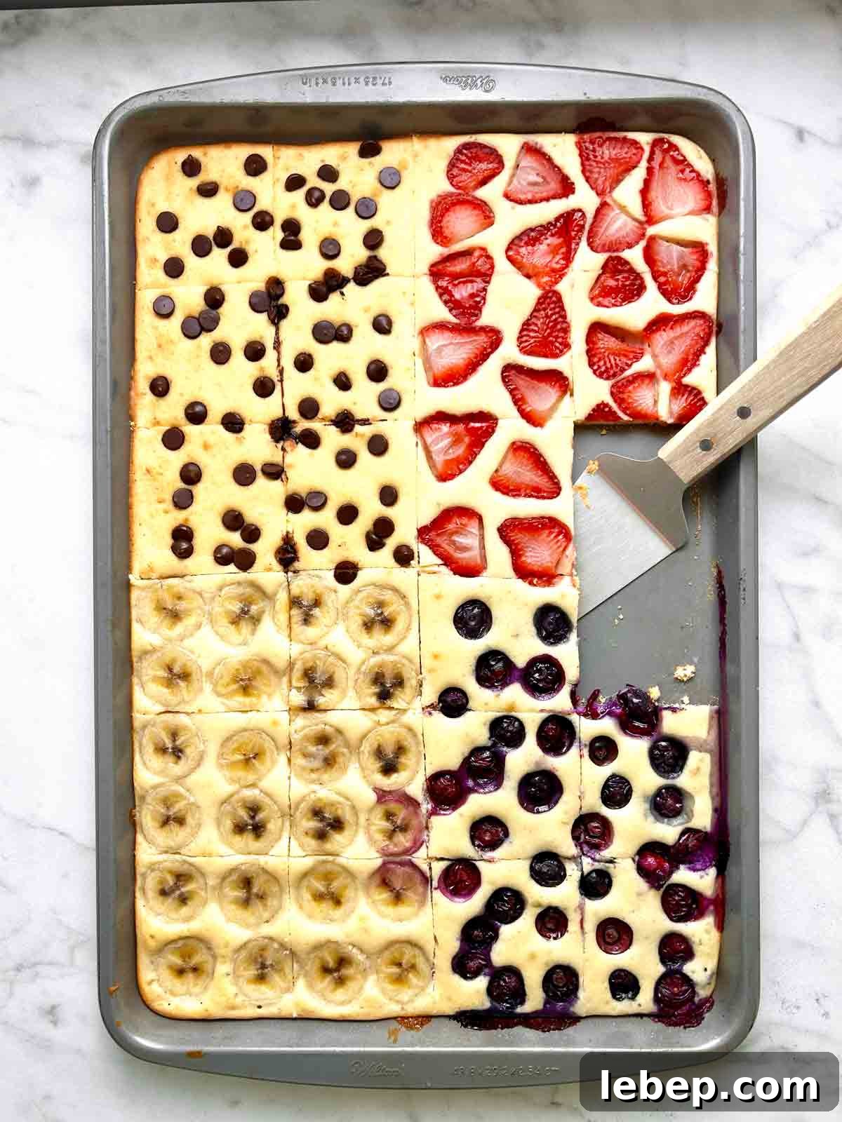 sheet pan pancakes cut into slices with spatula on pan.