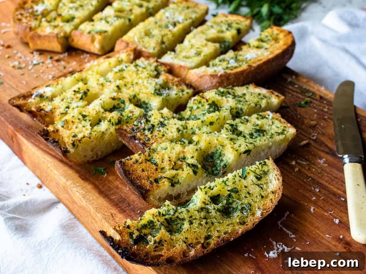 Crispy Ciabatta Garlic Bread Recipe with Herb Butter 5 Slices of toasted ciabatta with chopped green herbs on top on a wooden board.