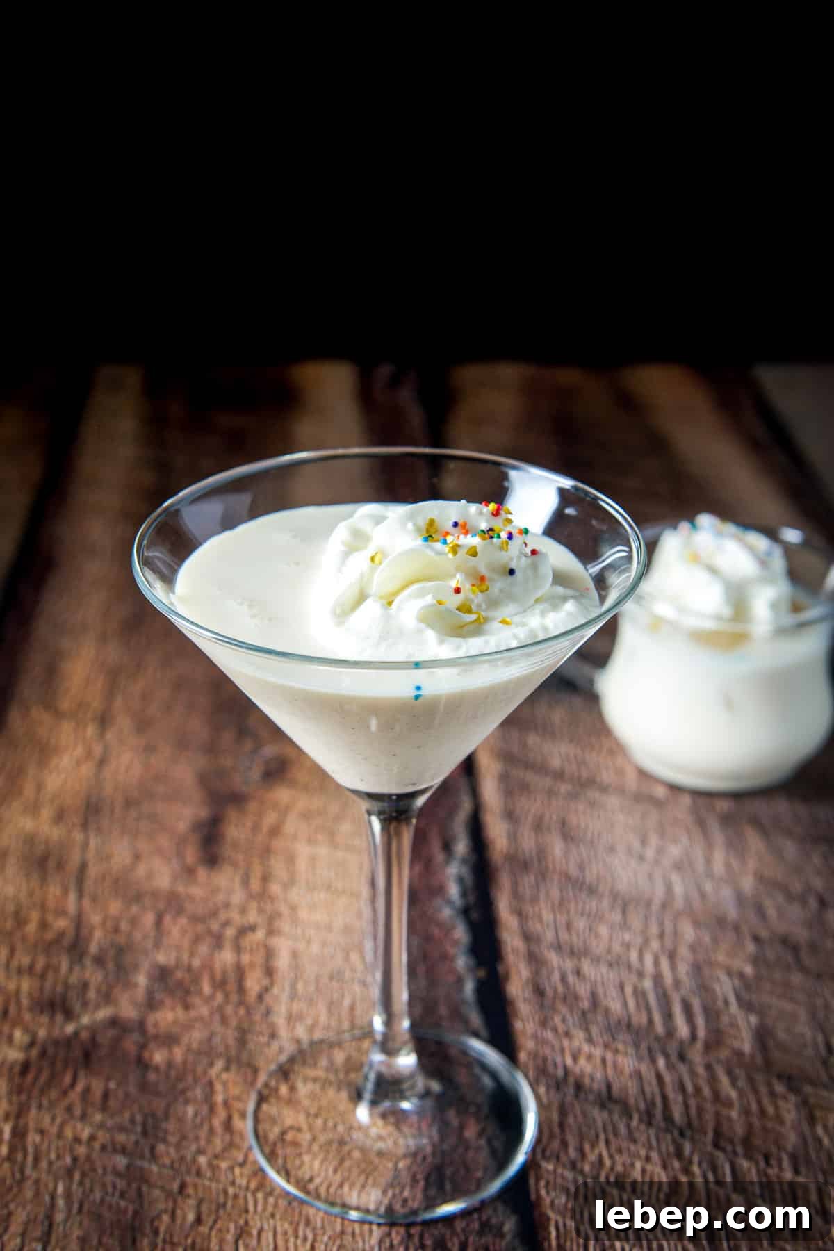 Mrs. Claus Cocktail Recipe: Festive Spiced Holiday Drink 2 Two glasses - a classic martini and a smaller glass filled with the creamy cocktail with whipped cream and sprinkles