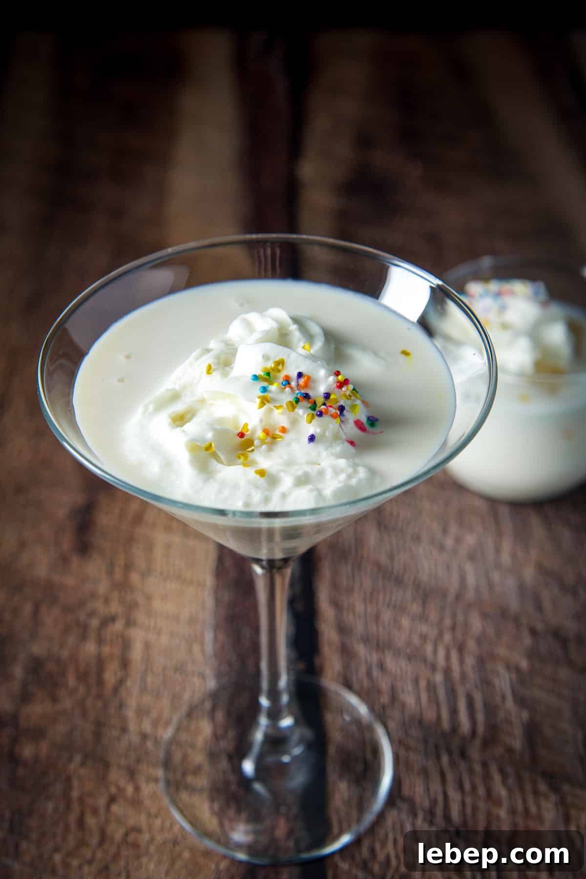 Mrs. Claus Cocktail Recipe: Festive Spiced Holiday Drink 6 Closer view of the martini glass filled with the white chocolate cocktail with whipped cream and sprinkles