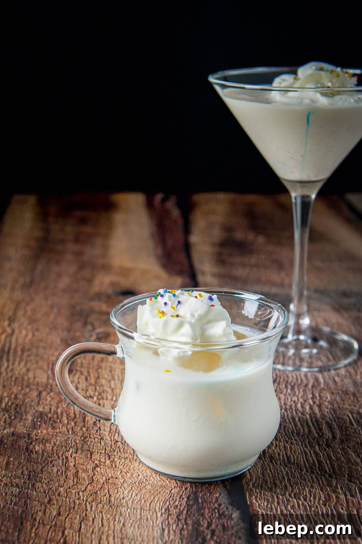 Mrs. Claus Cocktail Recipe: Festive Spiced Holiday Drink 7 A small handled glass with ice, the cocktail and whipped cream on it - with the classic martini in the back