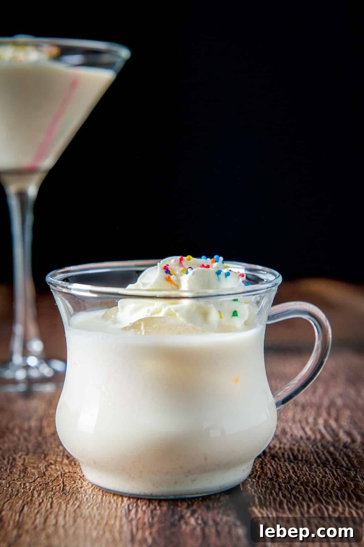 Mrs. Claus Cocktail Recipe: Festive Spiced Holiday Drink 9 vertical view with the egg nog drink with whipped cream and colored sprinkles
