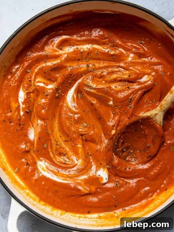 Tomato soup in a large pot with a wooden spoon. Pot is displayed on a white marble background.