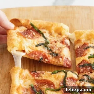 A hand pulling a slice of pepperoni stuffed crust tortilla pizza away from the whole pizza.