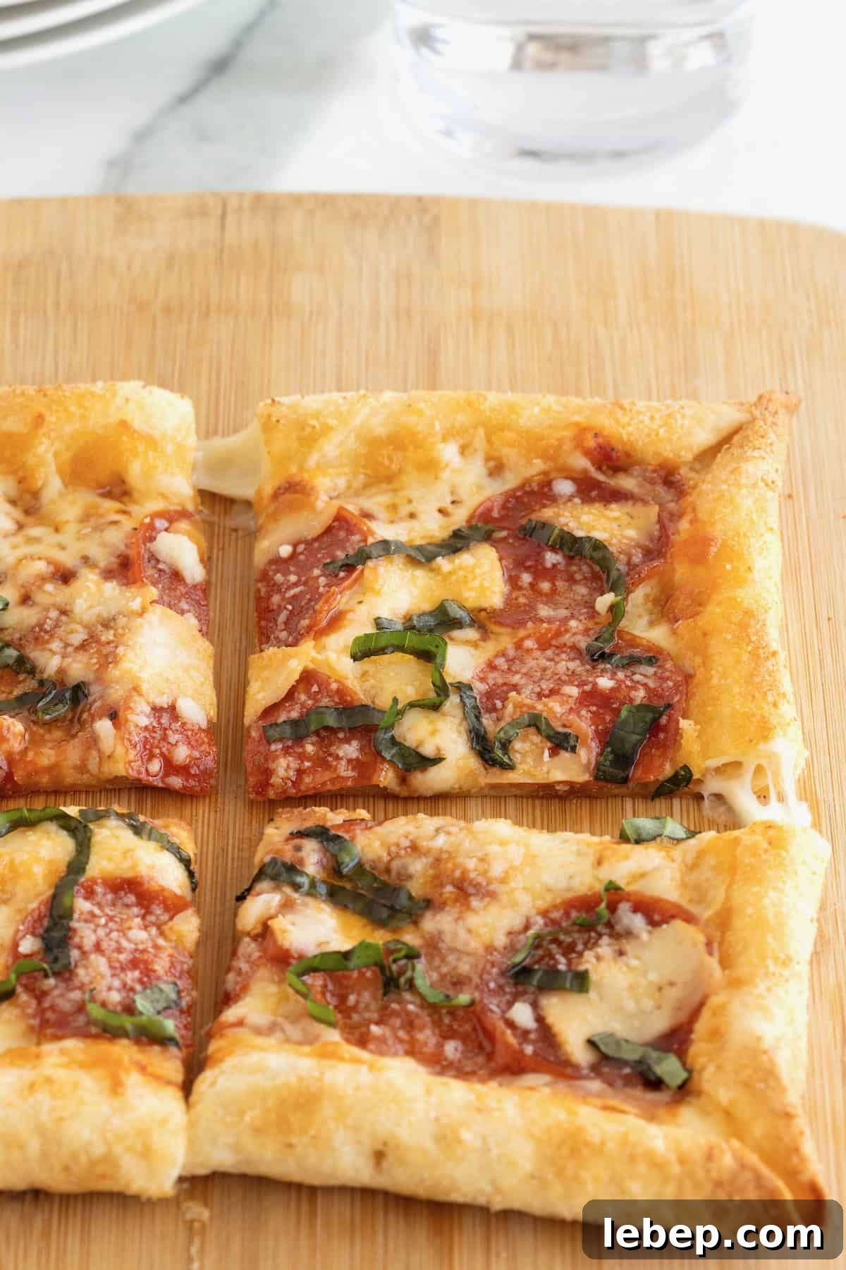 A stuffed crust tortilla pizza cut into four pieces on a rectangular light wood cutting board.