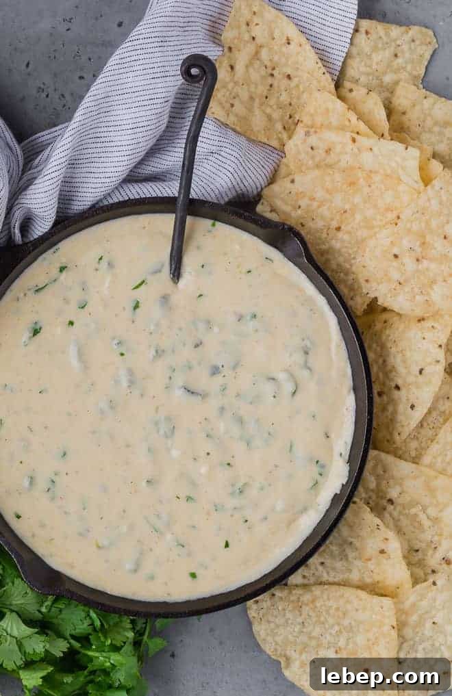 Creamy Poblano Queso Dip Recipe for Entertaining 4 Overhead view of queso made with poblano peppers, in a pan. Next to it are chips and fresh cilantro.