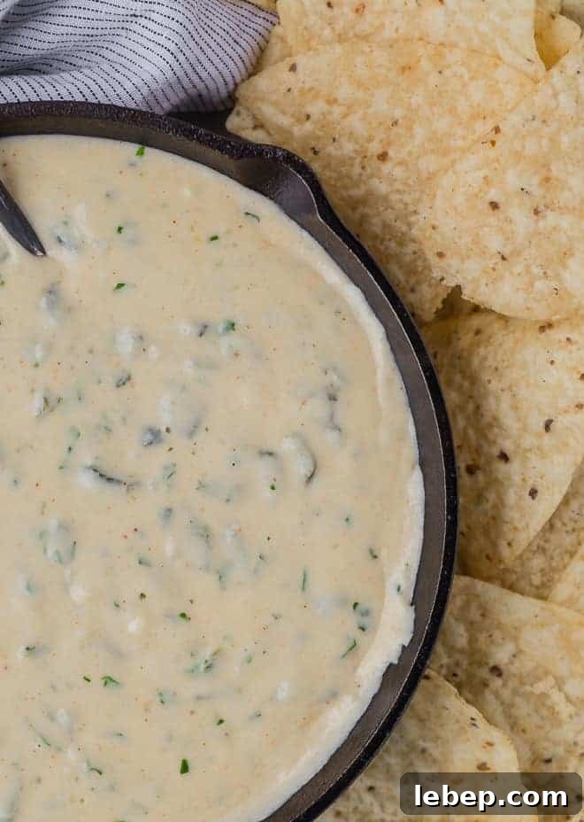 Creamy Poblano Queso Dip Recipe for Entertaining 5 Close up overhead view of queso in a black skillet, next to a pile of chips.