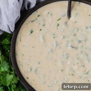 Creamy Poblano Queso Dip Recipe for Entertaining 7 Queso dip in a black pan with a black spoon, next to a black and white linen, and a bunch of fresh cilantro.