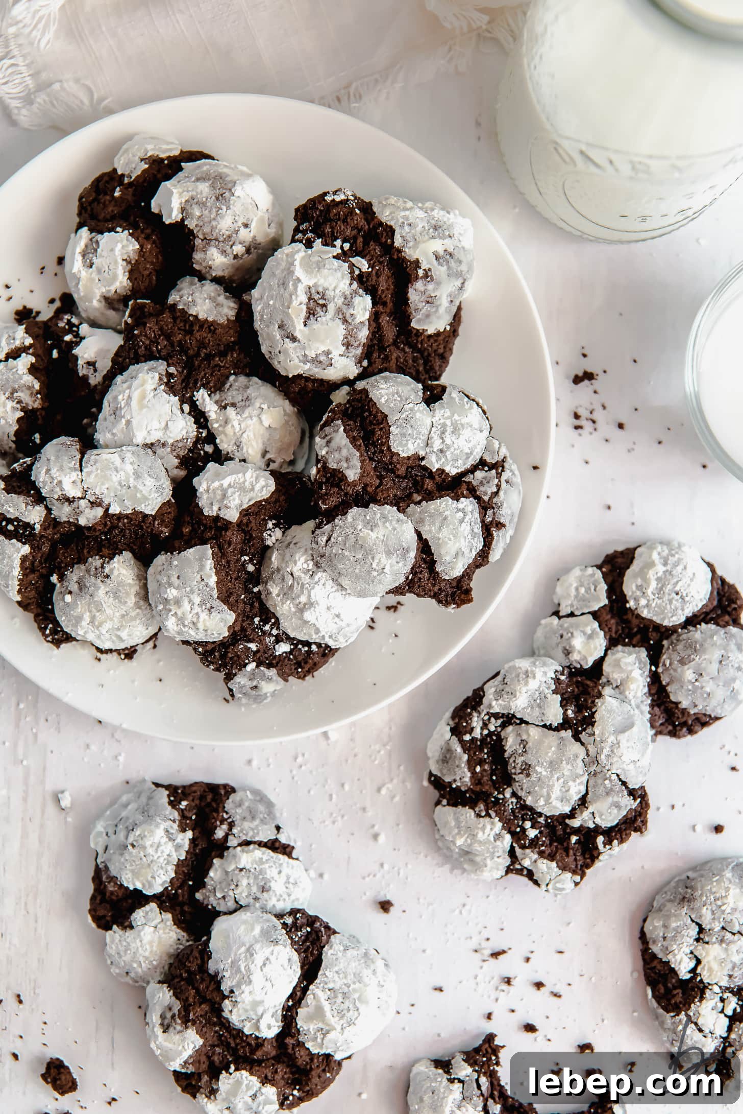 Chocolate Crinkle Cookies Recipe — Soft Fudgy Cookies in Minutes 2 chocolate crinkle cookies on white round plate next to more cookies and glass of milk