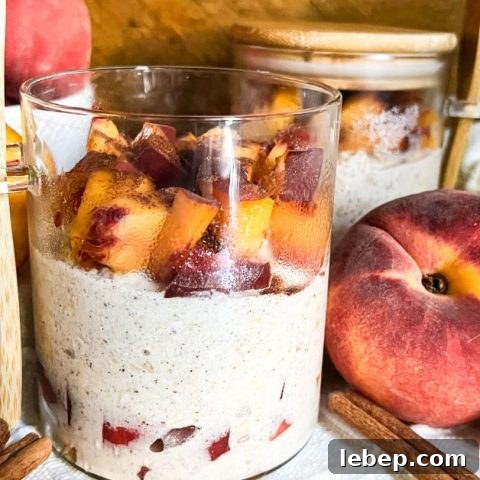 Jar of peach cobbler overnight oats surrounded by fresh peaches and sticks of cinnamon.