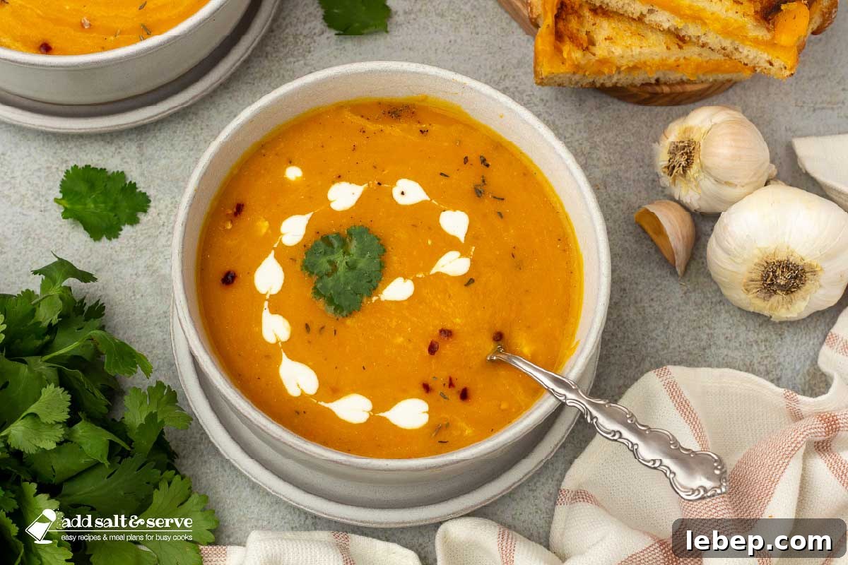 Carrot and Sweet Potato Soup with Ginger — Seasonal Comfort Bowl 2 Bowls of carrot sweet potato soup beside a cutting board with grilled cheese sandwiches with garlic bulbs and parsley to the side.