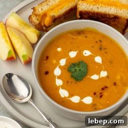 Carrot and Sweet Potato Soup with Ginger — Seasonal Comfort Bowl 7 Bowl of carrot sweet potato soup on a plate with apple slices and a grilled cheese sandwich.