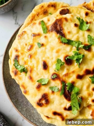Close up plate full of yoghurt naan bread brushed with butter and fresh coriander