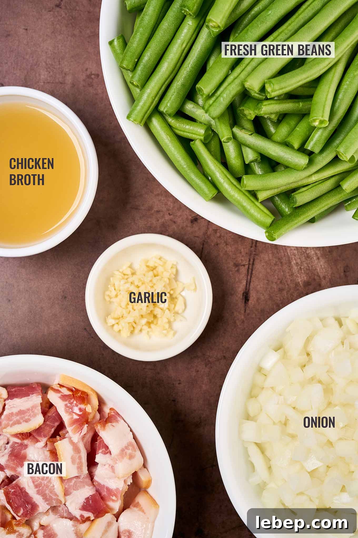 Southern-Style Green Beans with Bacon and Garlic 3 A labeled, overhead view of the ingredients needed for Southern style green beans including fresh green beans, bacon, garlic, onion, and chicken broth.