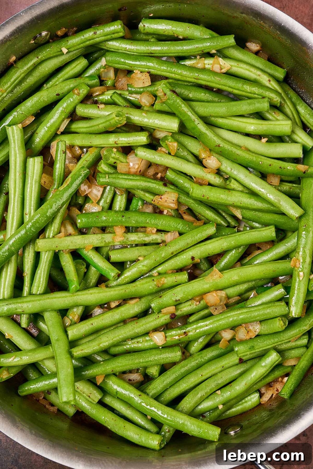 Southern-Style Green Beans with Bacon and Garlic 5 Trimmed, raw green beans in a sauté pan with sautéed onion and garlic, ready to be braised in chicken broth.