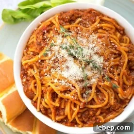 Spaghetti in a white bowl on plate with bread fork and green vegetable