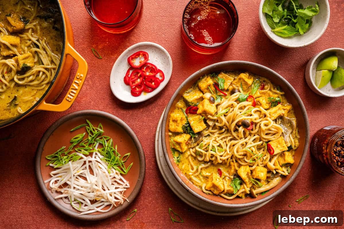 Malaysian curry noodle soup dinner scene on a red table.