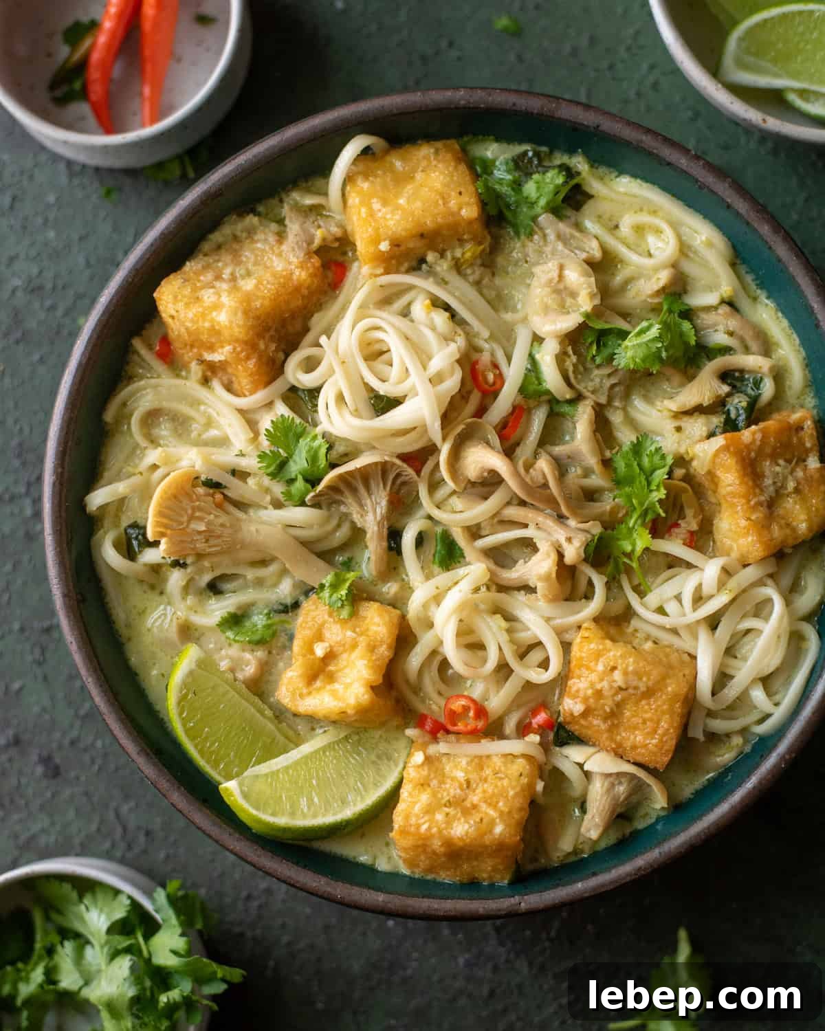 Malaysian curry noodle soup with fried tofu in a green bowl.