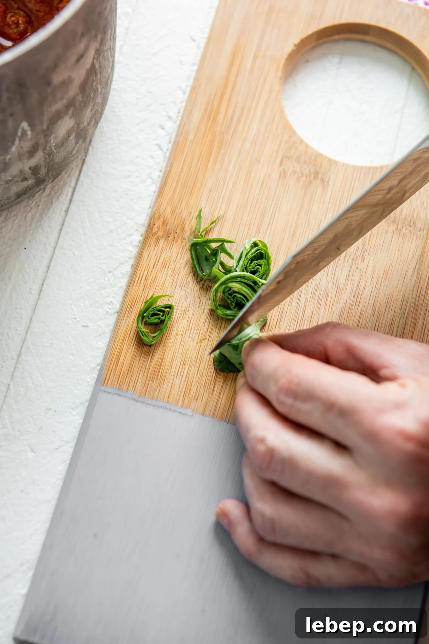 Cooking with Basil: 12 Flavorful Ways to Use Fresh Basil in Meals 7 Woman cutting basil into chiffonade strips on a painted cutting board.
