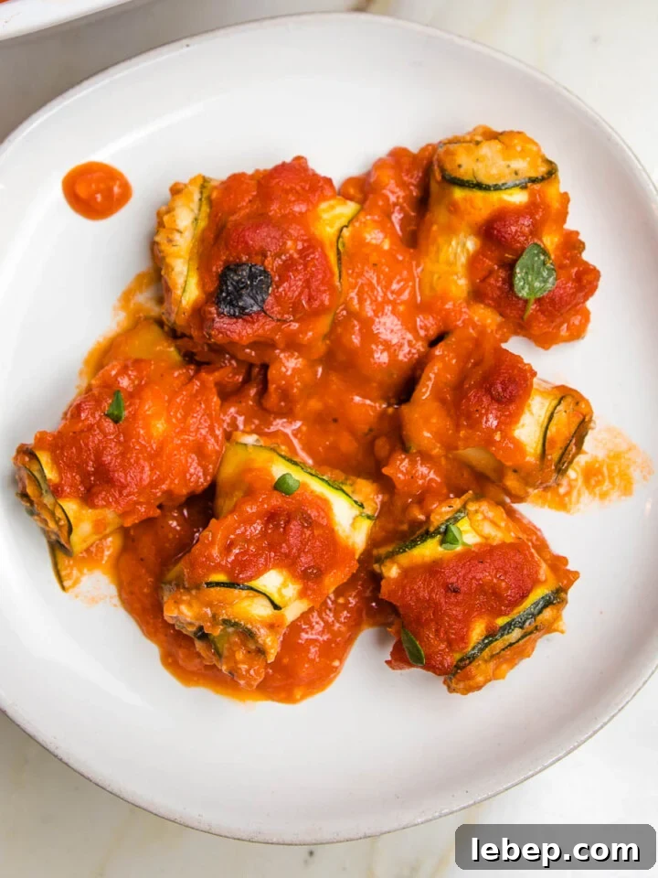 white rimmed plate with marinara sauce covered zucchini lasagna roll ups