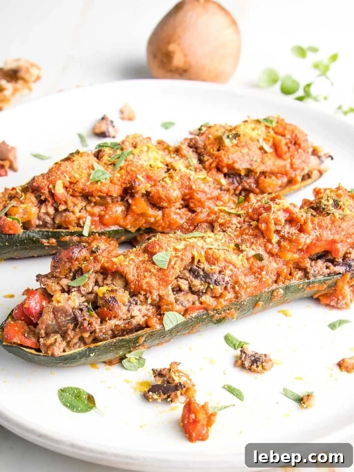 Rimmed white plate with 2 zucchini boats, stuffed with mushrooms and other chopped veggies.