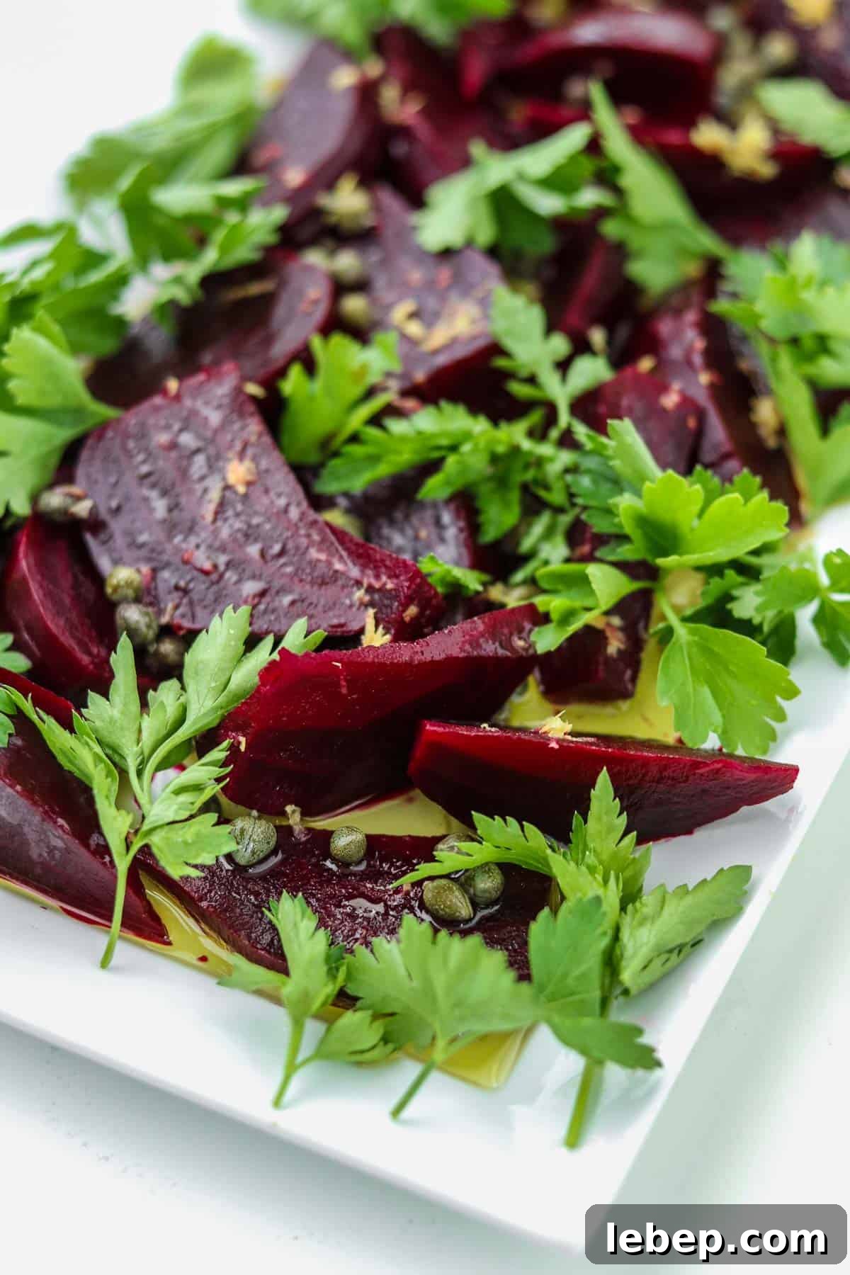 Beet salad on a white platter with parsley and capers.