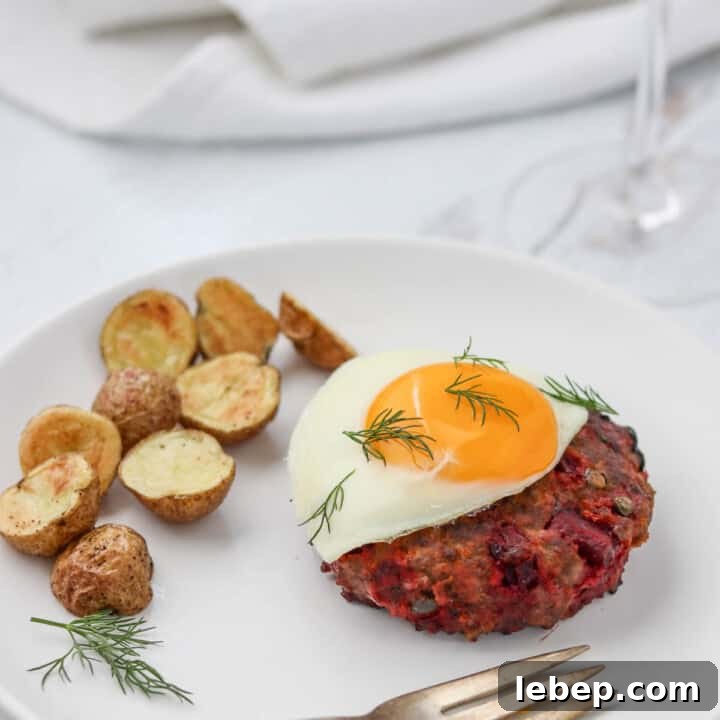 Beef Lindström on a plate topped with a fried egg next to roasted potatoes.
