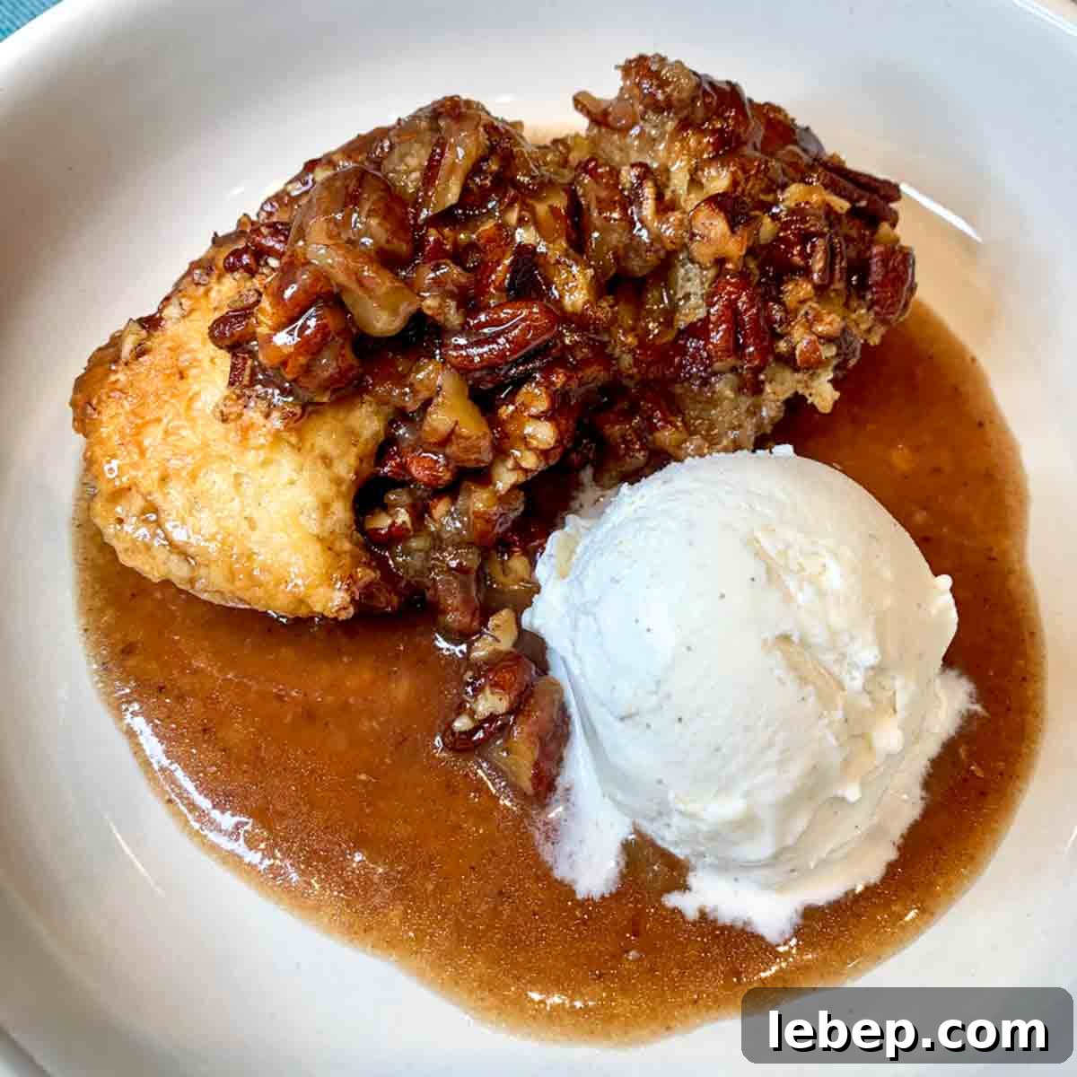 Pecan Pie Cobbler Recipe: Southern-Styled Gooey Pecan Dessert 16 A serving of pecan pie cobbler in a white bowl with a scoop of vanilla ice cream next to it.