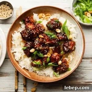 Bowl of kung pao crispy chicken with rice, topped with sesame seeds and peanuts.