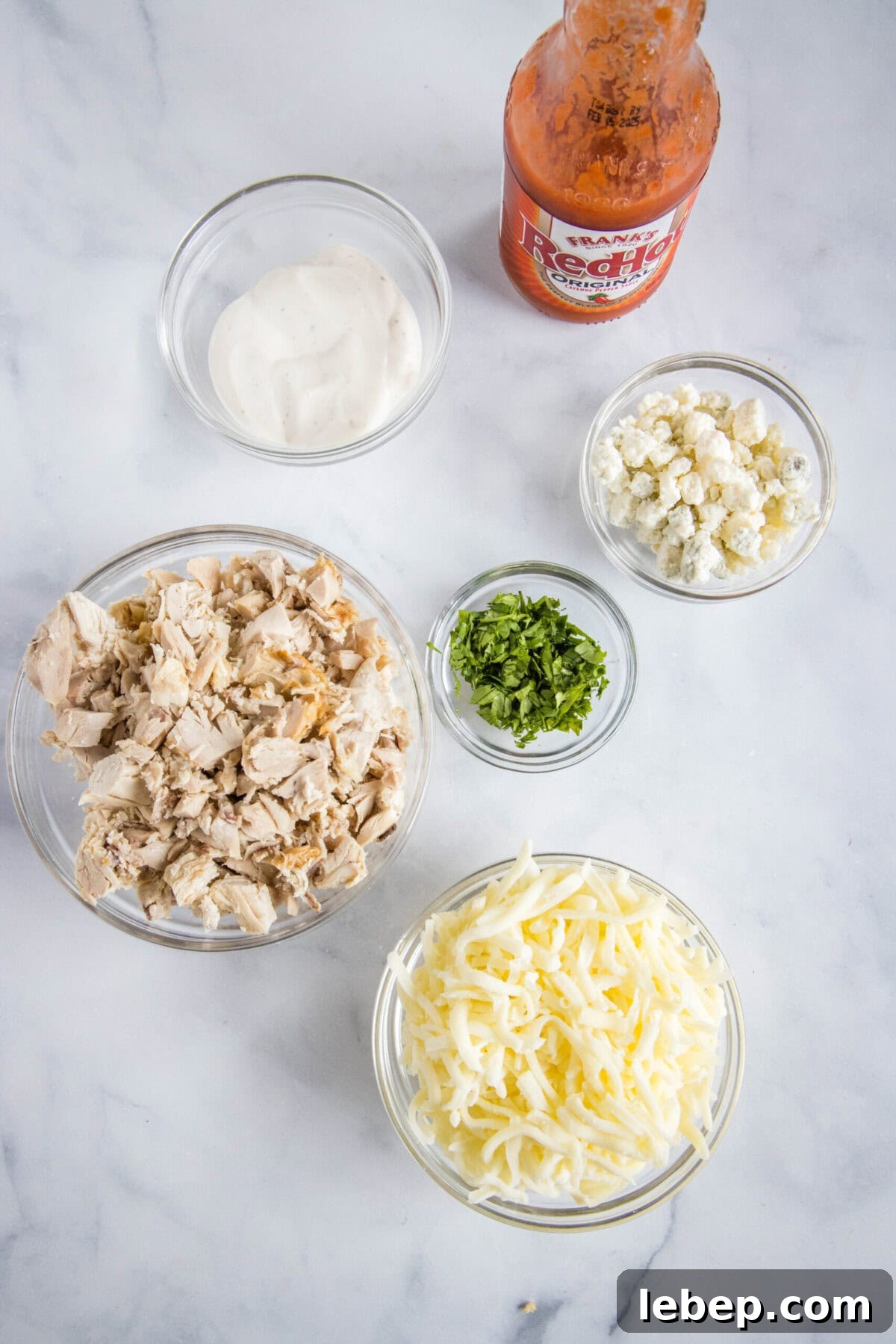 Homemade buffalo chicken pizza is loaded with spicy and juicy chicken, creamy ranch dressing, and melted cheese on a golden-brown crust. Overhead view of the ingredients needed for buffalo chicken pizza