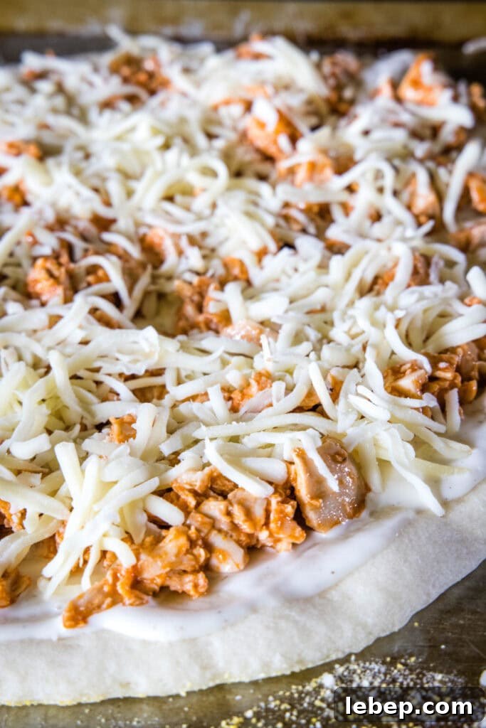 Assembled buffalo chicken pizza before baking. Unmelted cheese on top of buffalo chicken on top of ranch dressing on top of pizza dough
