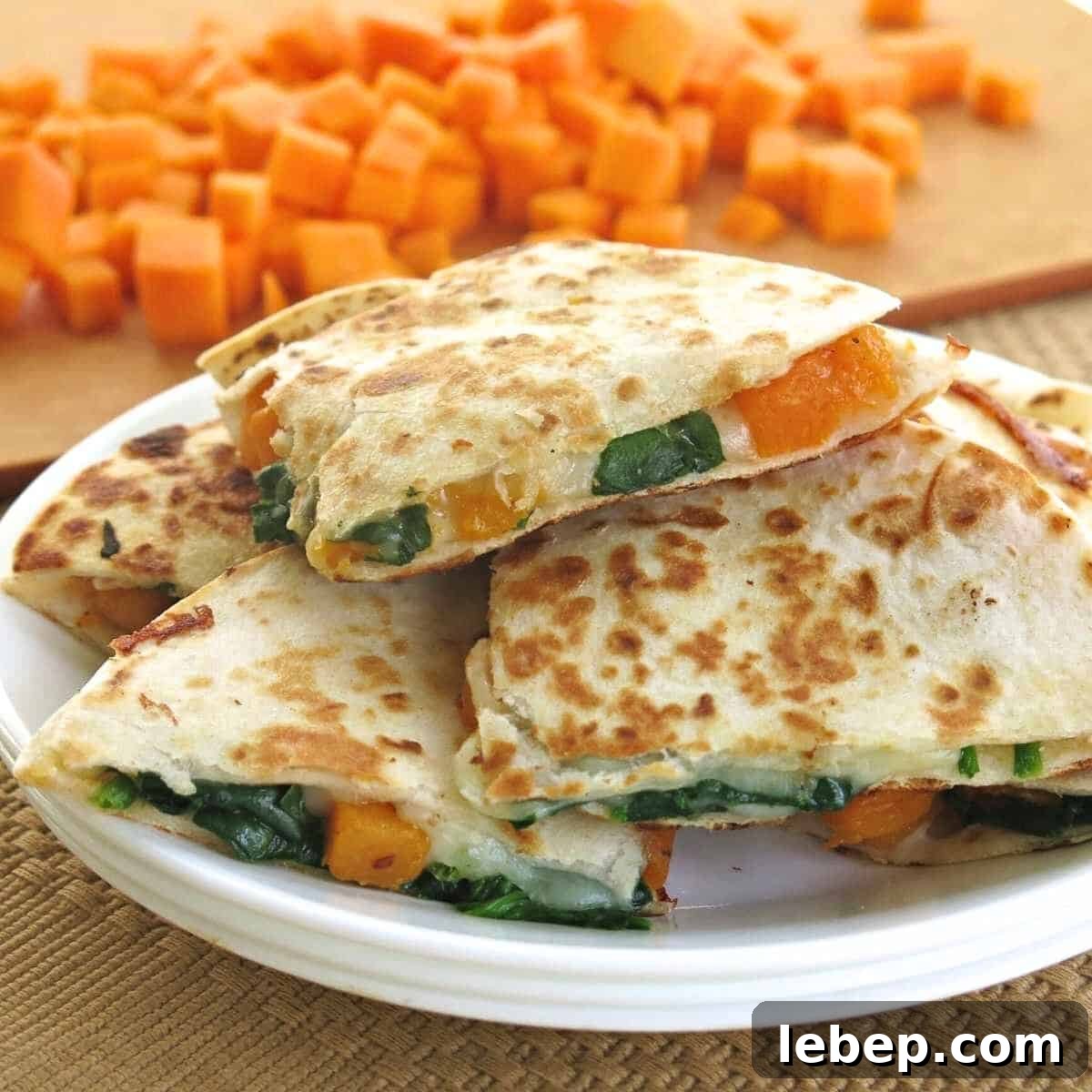 Butternut squash quesadillas piled on a plate with cubes of butternut squash in the background.