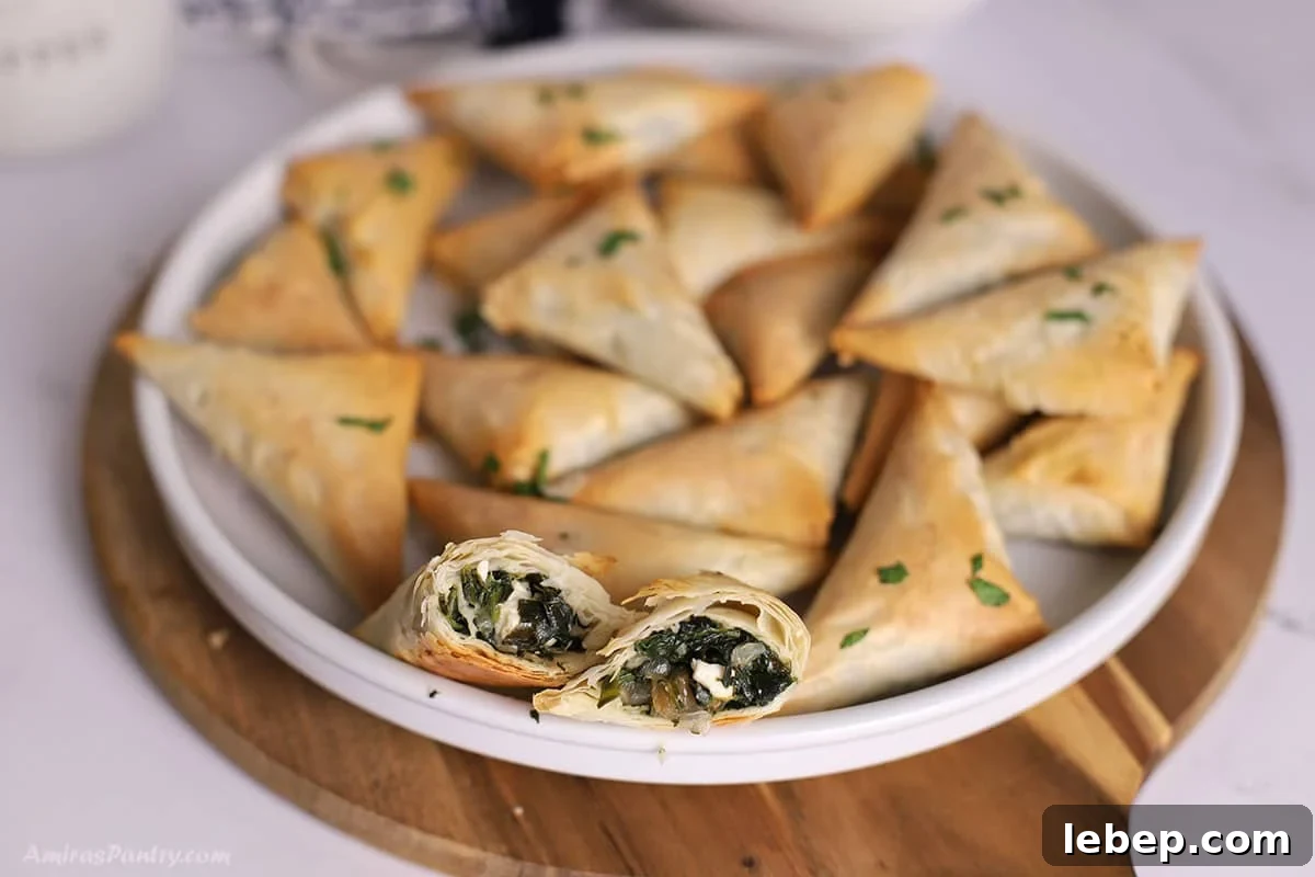 A white platter with spanakopita triangles with one cut in half to show texture.