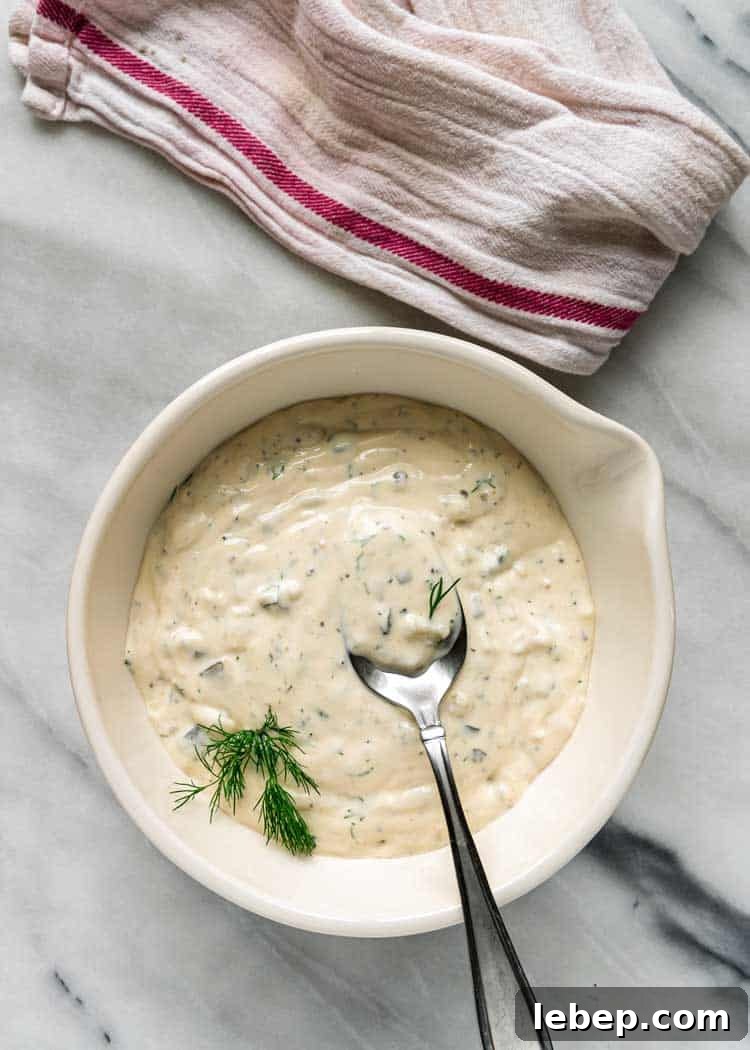 Classic Creamy Tartar Sauce Recipe for Fish and Seafood 5 closeup overhead: spoonful of tartar sauce over white bowl of tartar sauce