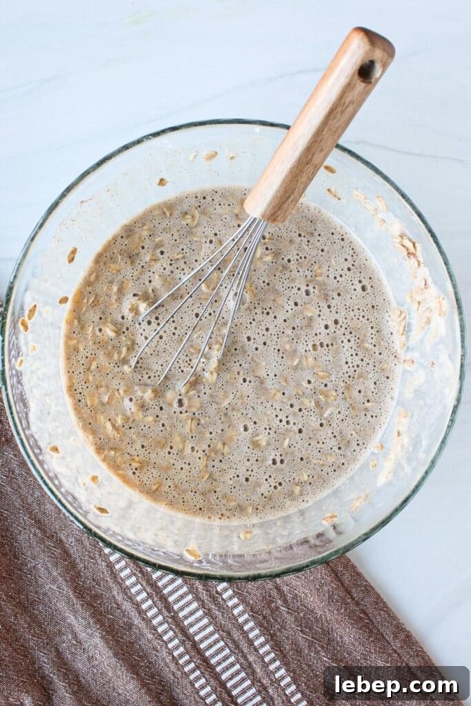 Cinnamon Roll Baked Oatmeal — Morning Bake with Creamy Glaze 5 A clear bowl with oatmeal, mashed banana, maple syrup and other ingredients for an oatmeal bake mixed.