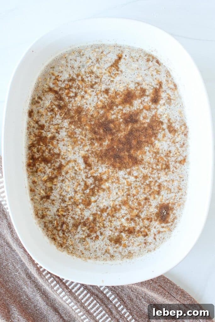 Cinnamon Roll Baked Oatmeal — Morning Bake with Creamy Glaze 7 A white casserole dish full of oats, mashed banana, eggs and other ingredients ready to go into the oven to be baked.
