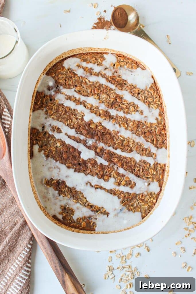 Cinnamon Roll Baked Oatmeal — Morning Bake with Creamy Glaze 8 A white casserole dish full of cinnamon oatmeal bake drizzled with a white sugar glaze.