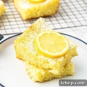 Bright yellow lemon bars stacked on a small white plate with a slice of lemon on top.