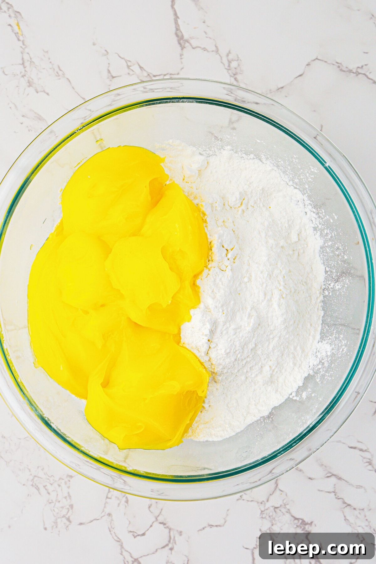 Cake mix and lemon pie filling being mixed together in a clear glass bowl.