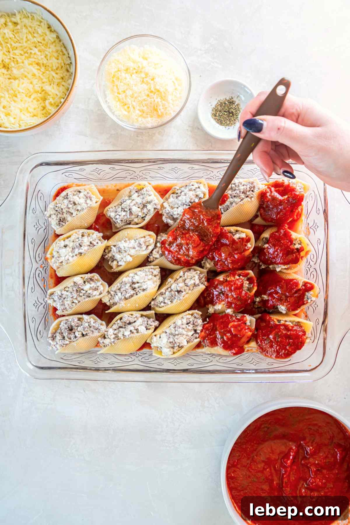 Baked Stuffed Shells with Beef and Cottage Cheese Filling 9 Stuffed shells arranged in baking dish with marinara sauce being added on top