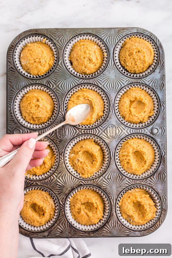 Fluffy Pumpkin Muffins with Cream Cheese Swirl 12 picture of a hand pressing a spoon into pumpkin batter in a muffin tin