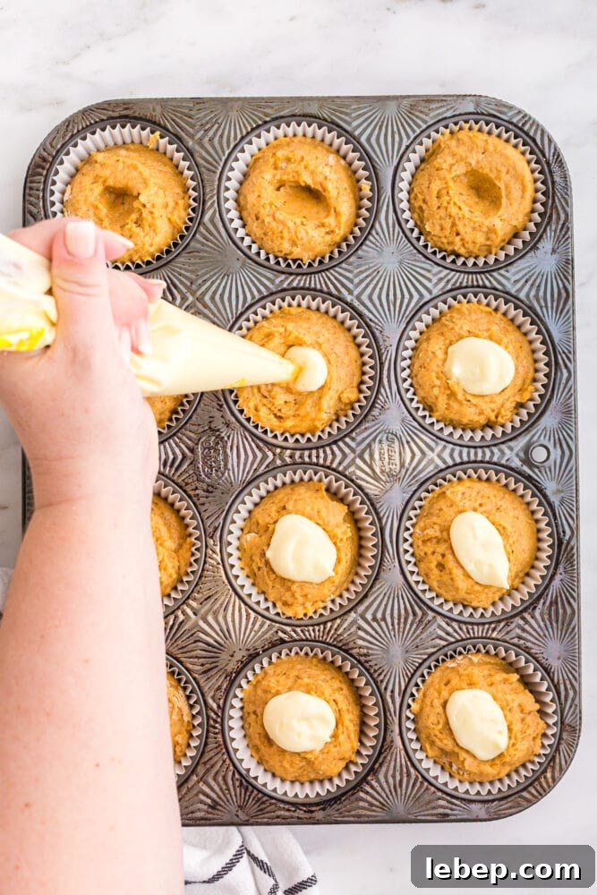 Fluffy Pumpkin Muffins with Cream Cheese Swirl 14 picture of hand piping cream cheese into dents on tops of muffins