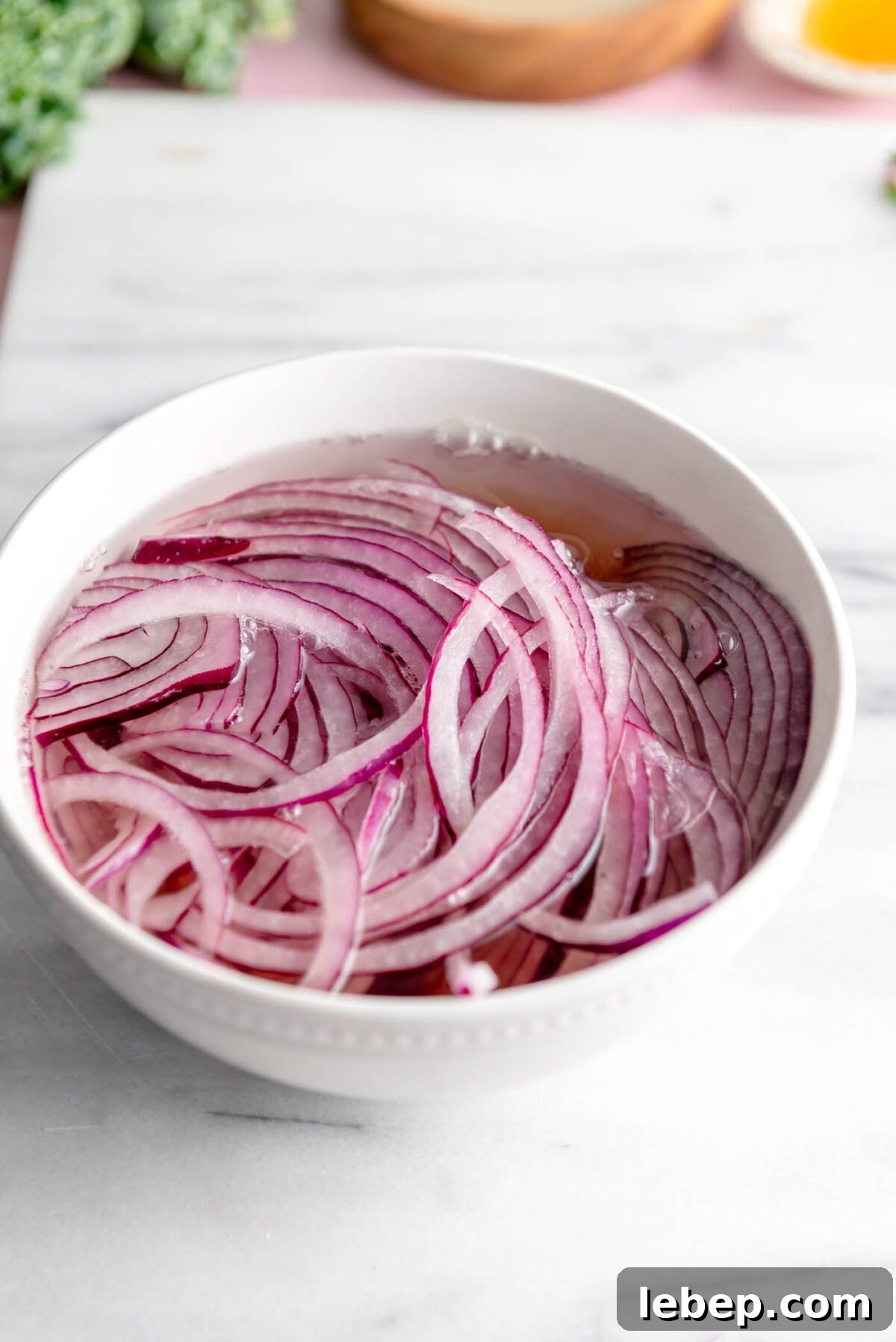 Thinly sliced red onion in water in a bowl.